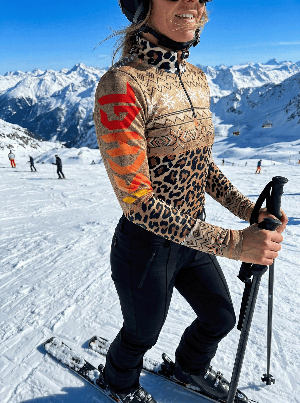Dames skiër in de sneeuw met Gutski Hüttenzauber panterprint skipully en oranje mouwprint